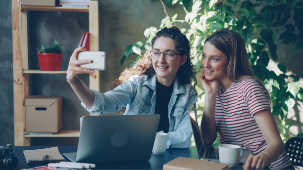 在现代化的办公环境中，年轻的企业家们正坐在办公桌前用智能手机聊天、自拍。他们摆着姿势，笑着图片下载