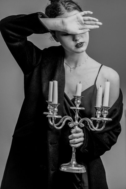 一个优雅的女性穿着吊带裙、风衣和烛台摆姿势的垂直灰度照片图片下载