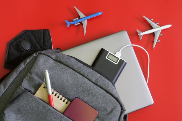 灰色背包和小工具:充电宝、手机、笔记本电脑、笔记本电脑和医用防护口罩。附近的玩具飞机。学生和记者的小工具和行李的概念图片下载