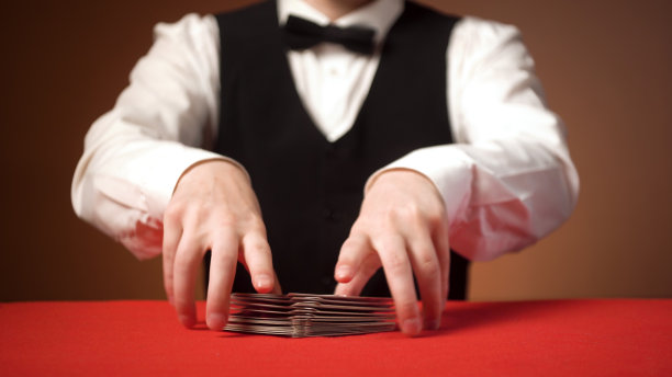 年轻的白人男性发牌者在游戏开始前洗牌。红色的表。图片下载