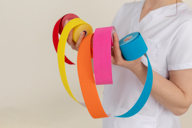 裁剪的照片按摩师穿着白色制服，持有显示多颜色的肌内西奥胶带卷在米色背景。图片下载