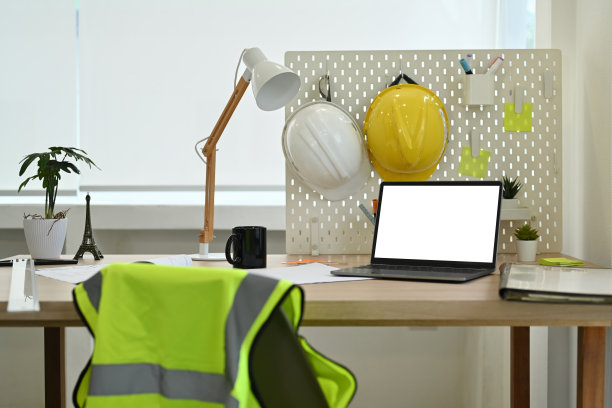 建筑师的办公桌，笔记本电脑，安全帽，反光夹克和文具。图片下载