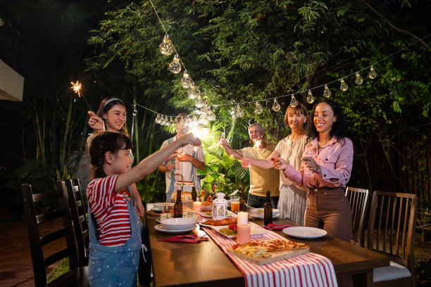 多民族大家庭在户外的花园中欢聚。迷人的各色人聚在餐桌前共进晚餐，吃着美食，庆祝周末团圆。图片下载
