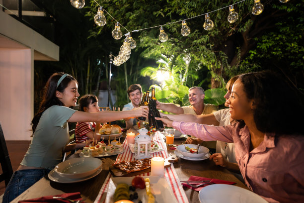 多民族大家庭在户外的花园中欢聚。迷人的各色人聚在餐桌前共进晚餐，吃着美食，庆祝周末团圆。图片下载
