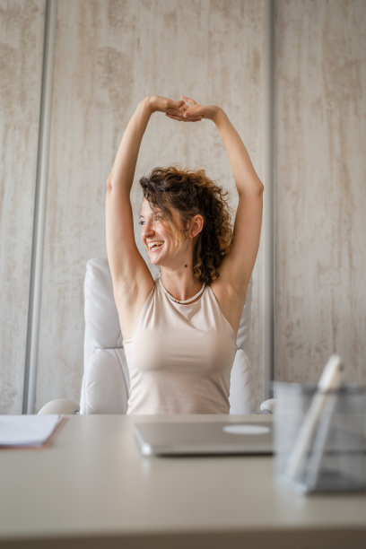年轻女子在早上工作时做伸展运动，而坐在桌子前背部疼痛图片下载