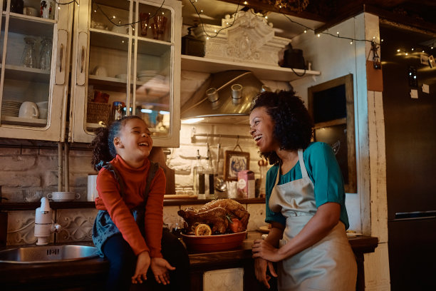 快乐的非裔美国母亲和女儿在厨房里准备感恩节午餐时大笑。图片下载