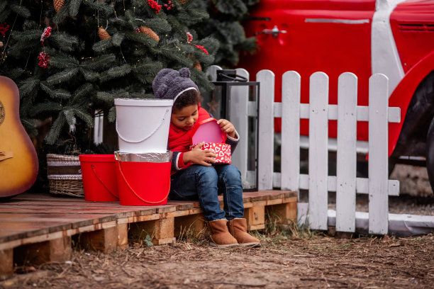 穿着熊装的非裔美国小男孩坐在圣诞树旁的木托盘上打开礼物图片下载