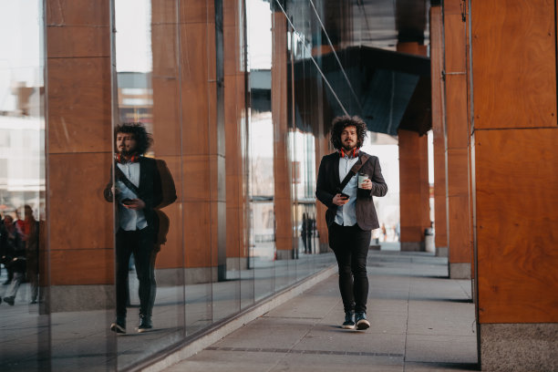时髦的商人带着皮制公文包在金融区用智能手机听着音频歌曲，戴着耳机喝着咖啡图片下载