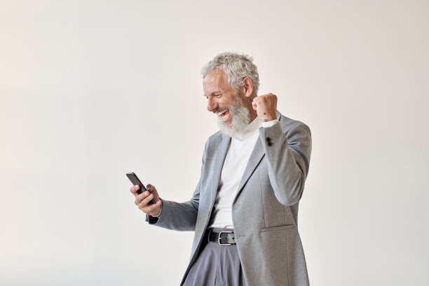 兴奋快乐的老商人投资者举起拳头使用智能手机。图片下载