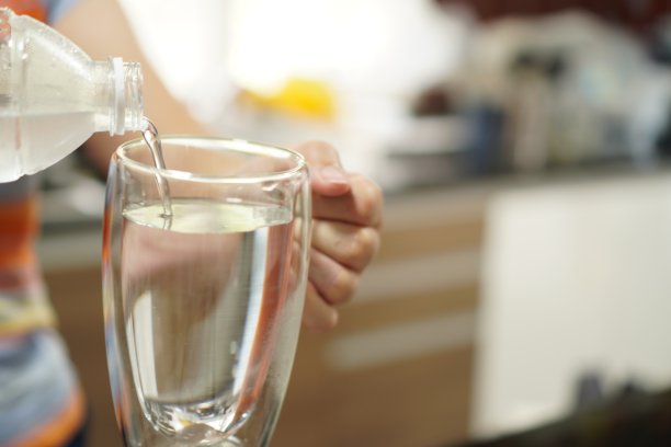 这张照片展示的是从一个瓶子里往玻璃杯里倒凉水，特写。图片下载