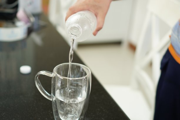 这张照片展示的是从一个瓶子里往玻璃杯里倒凉水，特写。图片下载