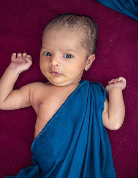 刚出生的宝宝躺在红色丝绒布上，从不同角度看表情可爱图片下载