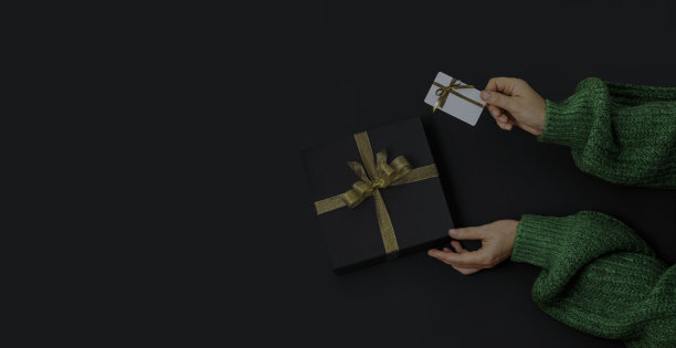 “黑色星期五”的概念。俯视图照片手黑色礼盒与金色丝带蝴蝶结和白色塑料卡在黑色背景与复制空间图片下载