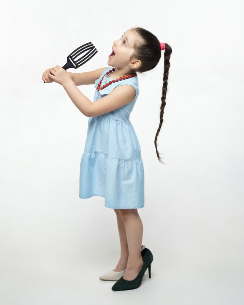 黑头发的小女孩玩着梳子，对着梳子唱歌。有趣的照片拍摄在工作室的白色背景图片下载