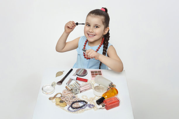 黑头发的小女孩在玩化妆。有趣的照片拍摄在工作室的白色背景图片下载