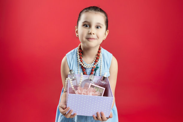 小黑头发的时尚达人手里拿着一包化妆品。一个女孩在摄影棚里用红色背景拍的有趣照片图片下载