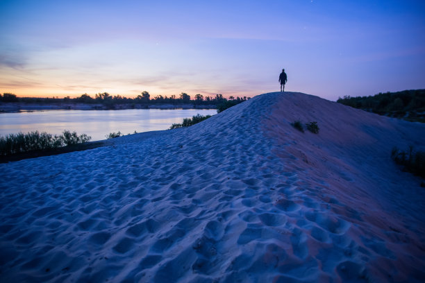 沙丘上的男人剪影。夏日早晨的天空。美丽的大气环境。长时间的曝光。《暮光之城》。黎明。河图片下载