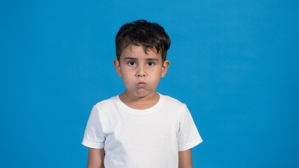 蓝色背景的快乐孩子，鼓着他的脸颊。他的呼吸图片下载