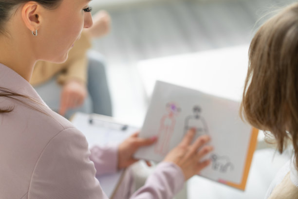 儿童心理学家的咨询。一个面目全非的孩子向专家解释这幅画。家庭关系。模糊的前景。图片下载