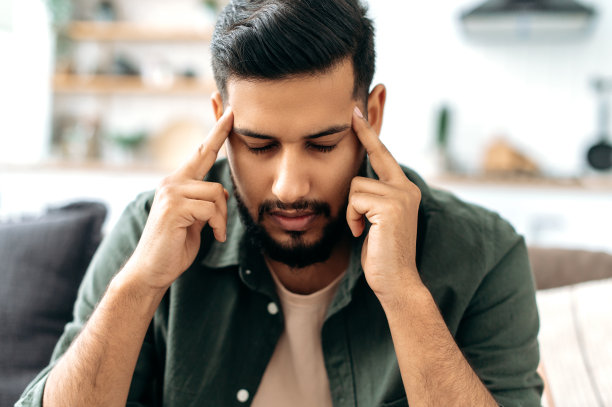 头痛、痉挛。悲伤疲惫的阿拉伯或印度青年男子，坐在客厅的沙发上，按摩太阳穴，闭上眼睛，感到不适，偏头痛，疲劳，需要治疗图片下载
