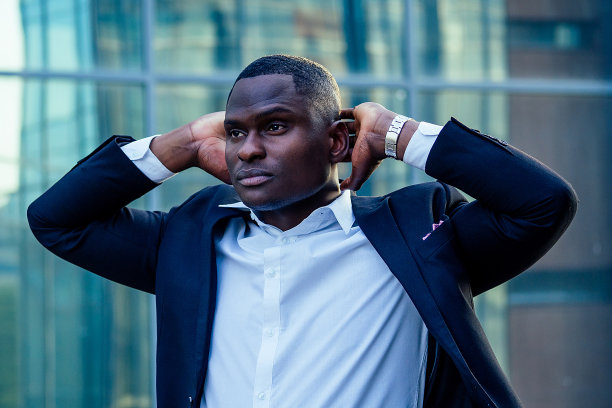 英俊的非洲裔商人穿着时髦的黑色西装，望向天空，在街道背景的办公室摩天大楼上祈祷。运气和成功交易的概念图片下载