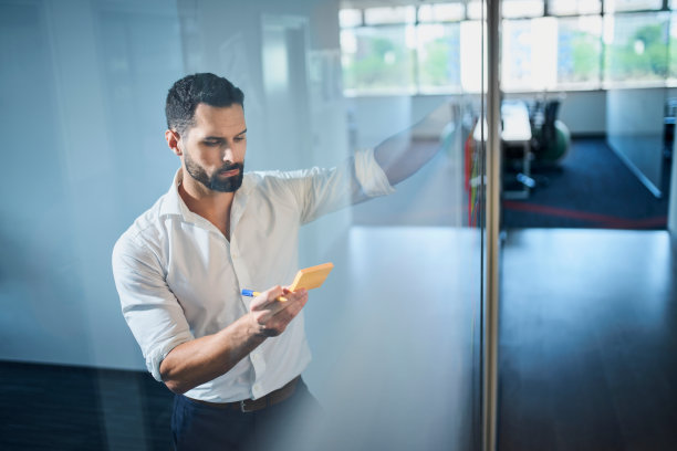 英俊的商人头脑风暴与笔记在玻璃墙上的现代办公室图片下载