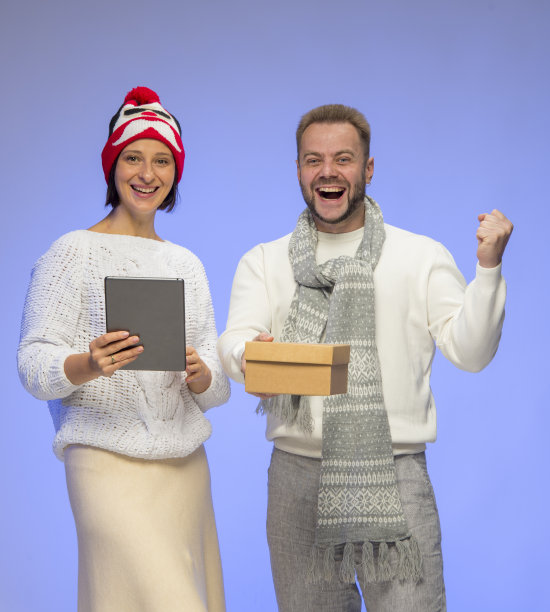 快乐的微笑的夫妇男人和女人礼品盒和智能手机平板电脑在蓝色背景的白色毛衣孤立。网上购物圣诞礼物概念图片下载