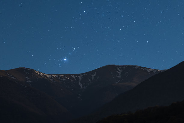 美丽的夜晚景观。白雪覆盖的山脉下星空与猎户座星系。图片下载