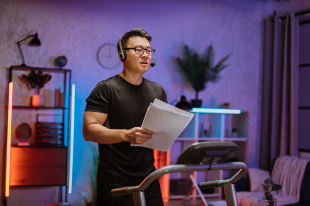 亚洲商人戴着耳机拿着纸在跑步机上锻炼图片下载