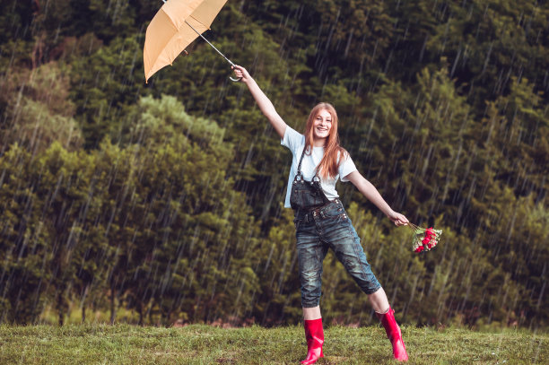 快乐的姜，带着黄伞，穿着红靴子的少女在雨中跳舞。图片下载