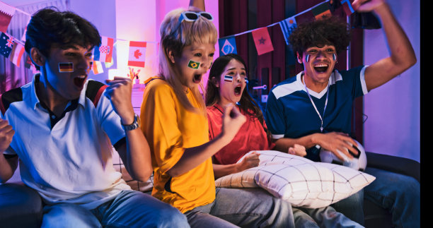 一群快乐的亚洲年轻人在家里看电视上的足球比赛，晚上一起欢呼庆祝进球。2022卡塔尔多哈世界杯，体育迷的支持者，或朋友聚会的概念图片下载