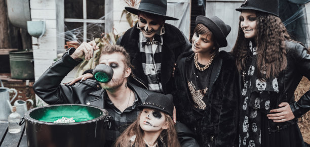 可怕的家庭，母亲，父亲，女儿们庆祝万圣节。药水的大锅。可怕的黑色骷髅半脸妆，女巫服装，时髦的图片。恐怖，有趣的孩子在牲口棚在街上的聚会图片下载