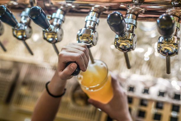 在酒吧或酒吧里，女酒保手拿着啤酒龙头，将桶装啤酒倒进玻璃杯里图片下载