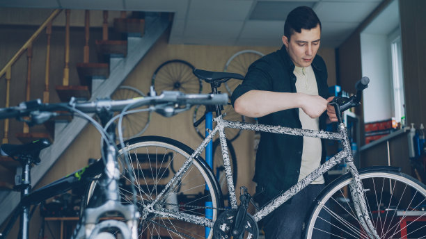 有经验的师傅在车间工作，用专用工具检查和修理自行车车把，车间有大量的零部件和设备。图片下载