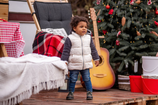 穿着冬季背心和牛仔裤的非洲裔小女孩站在拖车家附近的木托盘上。图片下载