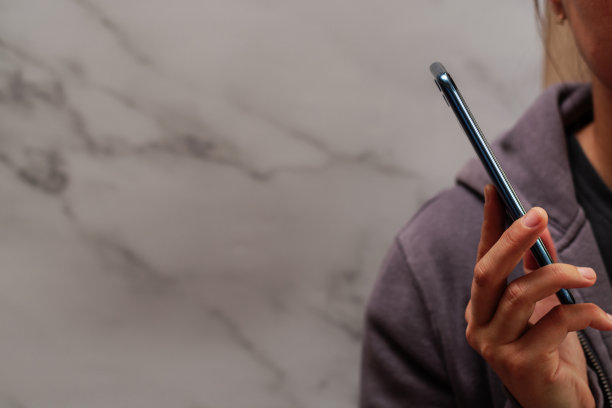 一个女人手里拿着一个蓝色的电话。大理石的背景。图片下载