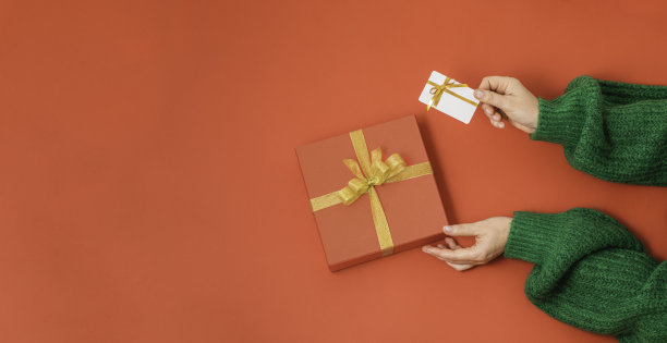 平的。手握红色礼盒与金色缎面缎带蝴蝶结和白色塑料卡上孤立的红色背景与复制空间图片下载