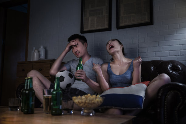 一对夫妻晚上在客厅沙发上看电视上的足球比赛，他们支持的球队输了比赛，他们有失望的表情——库存照片图片下载