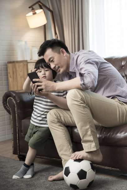 父子俩坐在客厅的沙发上，用智能手机看足球比赛。- - -库存图片图片下载
