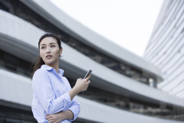 年轻的商业女性在职业装，寻找她的目的地与她的手机，迷失在建筑物之间-库存照片图片下载