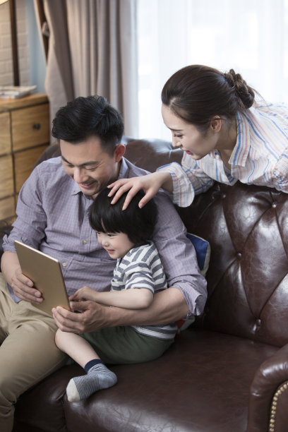 一家三口坐在客厅沙发上使用平板电脑。- - -库存图片图片下载