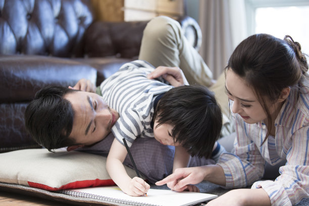 一家三口在客厅里玩耍。小男孩躺在他父亲的身上，画着库存照片图片下载