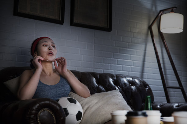 深夜在客厅沙发上看电视上的足球比赛的女士带着库存照片的保湿面膜图片下载