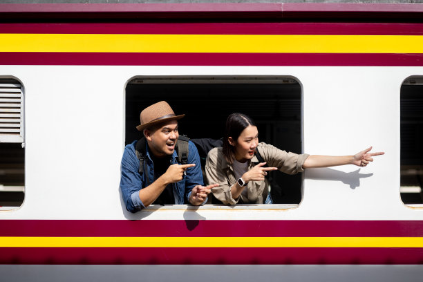 一对亚洲旅行者带着旅行包坐火车蜜月旅行把头伸出窗外。站台附近的快乐男人和女人。计划旅游的假期时间，假期，周末。图片下载