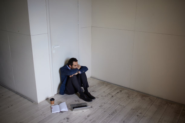 年轻商人的画像坐在空房间的地板上。业务关闭。萧条和危机。感到悲伤和无助图片下载