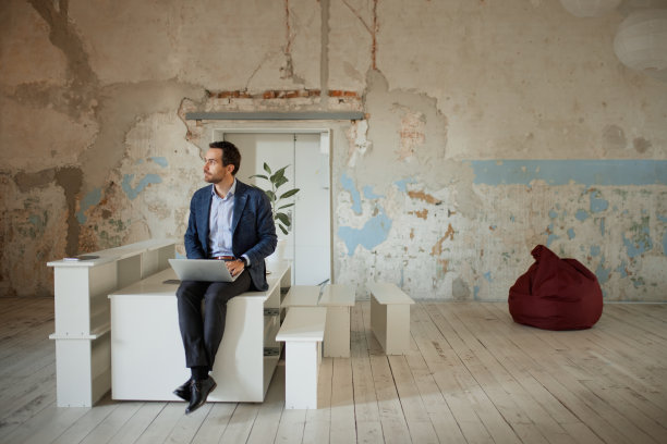 画像的年轻人，建筑师坐在空的房间和笔记本电脑上工作，使项目进一步的公司建设图片下载