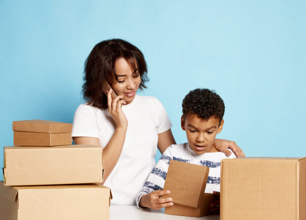 画像上的女人在打电话和十几岁的男孩打开盒子孤立的蓝色背景。网上购物图片下载