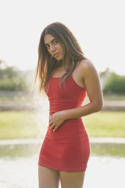 女孩穿着紧身的红色连衣裙和长长的直发在公园摆姿势图片下载
