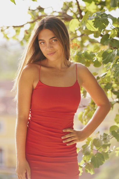 女孩穿着紧身的红色连衣裙和长长的直发在公园摆姿势图片下载