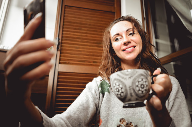 拿着智能手机的女性在家喝杯热茶或咖啡放松图片下载